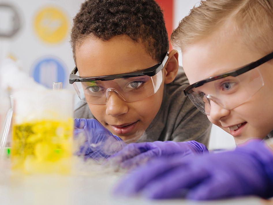 PIcture of two kids in front of a beaker of yellow liquid